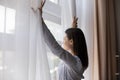 Happy young woman opening curtains, looking out of window. Royalty Free Stock Photo