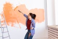 Dancing funny woman painting wall in her new apartment. Renovation, redecoration and repair concept. Royalty Free Stock Photo