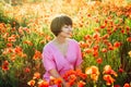 A happy young woman in a pink dress with closed eyes, relaxing in red poppies flowers meadow in sunset light. A simple pleasure