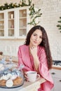 Happy young woman in pink dress with cup in Christmas decorated kitchen. beautiful brunette with cup of cocoa in kitchen with Royalty Free Stock Photo