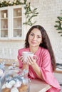 Happy young woman in pink dress with cup in Christmas decorated kitchen. beautiful brunette with cup of cocoa in kitchen with Royalty Free Stock Photo