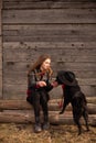 Happy young woman plaing with her black dog in fron of old wooden house. Girl tries a hat to her dog Royalty Free Stock Photo