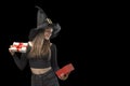 Happy young woman in pointed witches hat with opened gift in hands. Copy space. Isolation on black background. Halloween