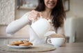 Happy young woman pouring herbal tea in mug, sitting at table in kitchen interior, selective focus Royalty Free Stock Photo