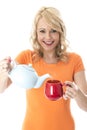 Happy Young Woman Pouring Tea from a Teapot Into Red Mug Royalty Free Stock Photo