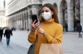 Happy young woman in protective mask holding shopping bags using smartphone on city street Royalty Free Stock Photo