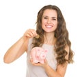 Happy young woman putting coin into piggy bank