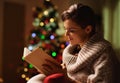 Happy young woman reading book in front of christmas tree Royalty Free Stock Photo