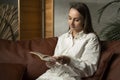 Happy young woman is reading a book at home on the couch. Freelancer lifestyle relax and unwind in the living room. Royalty Free Stock Photo