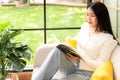 Happy young woman reading book on sofa at home. Lifestyle freelance relax and chill drinking coffee in living room Royalty Free Stock Photo