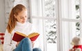 Happy young woman reading a book by window in winter Royalty Free Stock Photo