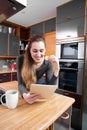 Happy young woman reading her connected tablet, eating in kitchen