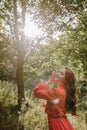 Happy young woman in red dress and with red long curly hair reaching out her hands to the sun in the forest Royalty Free Stock Photo