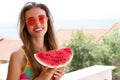 Happy young woman in red sunglasses and a swimsuit holds a piece of watermelon on a background of sea and beach Royalty Free Stock Photo