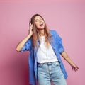 Happy young woman relaxed with great song, has broad smile, touches headphones, listens music, dressed in blue casual shirt Royalty Free Stock Photo