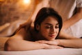 Happy young woman relaxing during back massage in spa with soft light, close-up.