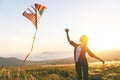 Happy young woman running with kite on glade at sunset in summer Royalty Free Stock Photo