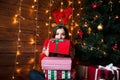 Happy young woman in santa hat opening gift box at golden beautiful christmas tree with lights at home Royalty Free Stock Photo