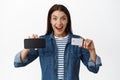 Happy young woman showing horizontal mobile phone screen and discount credit card, smiling excited, recommending sale or