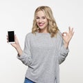 Happy young woman showing mobile phone with blank screen over white background, making ok sign with her hand. Royalty Free Stock Photo