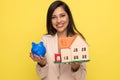 Happy young woman showing piggy bank and building model Royalty Free Stock Photo