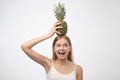 Happy young woman showing pineapple holding it on head. Concept of healthy veggie diet.