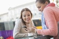 Happy young woman showing text message to friend at sidewalk cafe