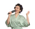 Happy young woman in silk bathrobe with hair curlers singing into hairbrush on white background Royalty Free Stock Photo