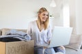 Happy young woman sit on couch stuck clothes in donation box at home, caring biracial female volunteer put apparel in carton Royalty Free Stock Photo