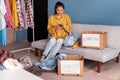 Happy young woman sit on couch stuck clothes in donation box at home, caring female volunteer put apparel in carton Royalty Free Stock Photo