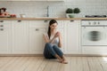 Happy young woman sit on kitchen floor using modern smartphone Royalty Free Stock Photo