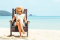 Happy young woman sitting on beach chair on tropical beach in white dress Royalty Free Stock Photo