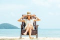 Happy young woman sitting on beach chair on tropical beach in white dress Royalty Free Stock Photo