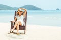 Happy young woman sitting on beach chair on tropical beach in white dress Royalty Free Stock Photo