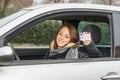 Happy young woman sitting in the car smiling at the camera showing her driver license