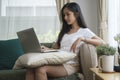 Happy young woman sitting on couch in living room and using laptop computer Royalty Free Stock Photo