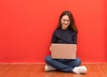 Happy young woman sitting on the floor with crossed legs and using laptop on gray background Royalty Free Stock Photo