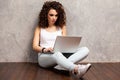 Happy young woman sitting on the floor with crossed legs and using laptop on gray background. Royalty Free Stock Photo