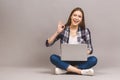 Happy young woman sitting on the floor with crossed legs and using laptop isolated on gray background. Ok sign Royalty Free Stock Photo