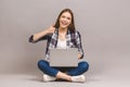 Happy young woman sitting on the floor with crossed legs and using laptop isolated on gray background. Thumbs up Royalty Free Stock Photo