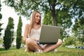 Happy young woman, sitting on grass, chatting with family using laptop, smiling broadly looking at camera against Royalty Free Stock Photo