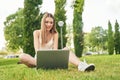 Happy young woman, sitting on grass, chatting with family using laptop, smiling broadly looking at camera against Royalty Free Stock Photo