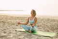 A happy young woman is sitting in a lotus position and doing yoga on the beach at sunset. The concept of a healthy Royalty Free Stock Photo