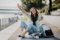 Happy young woman sitting on skateboard and listening music at city bridge. Youth culture and commuting concept. Royalty Free Stock Photo