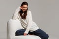 Happy young woman sitting on sofa at home and looking at camera. Portrait of comfortable woman in winter clothes relaxing on Royalty Free Stock Photo