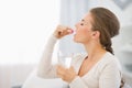 Happy young woman sitting on sofa and taking pill Royalty Free Stock Photo