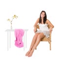 Happy young woman sitting on a wicker chair beside a table with a beautiful flower in a vase and a pink towel Royalty Free Stock Photo