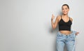 Happy young woman with slim body in oversized jeans on light background, space for text. Weight loss