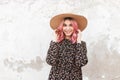 Happy young woman with smile with glamour pink hair in fashion vintage straw hat in black stylish beautiful floral dress near wall Royalty Free Stock Photo