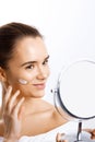 Happy young woman smiling, looking on mirror and applying cream to her face Royalty Free Stock Photo